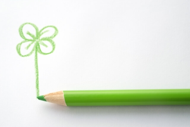 緑色の色鉛筆から四葉のクローバーが生えた写真